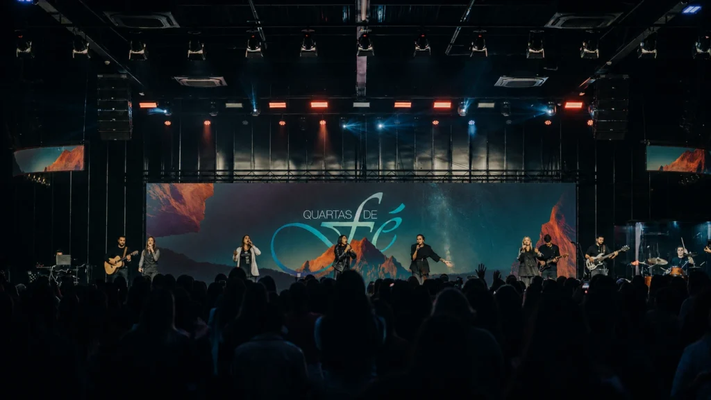 Registro do encontro Quartas de Fé na igreja, com participantes no palco, público e identidade visual exibida no telão ao fundo.