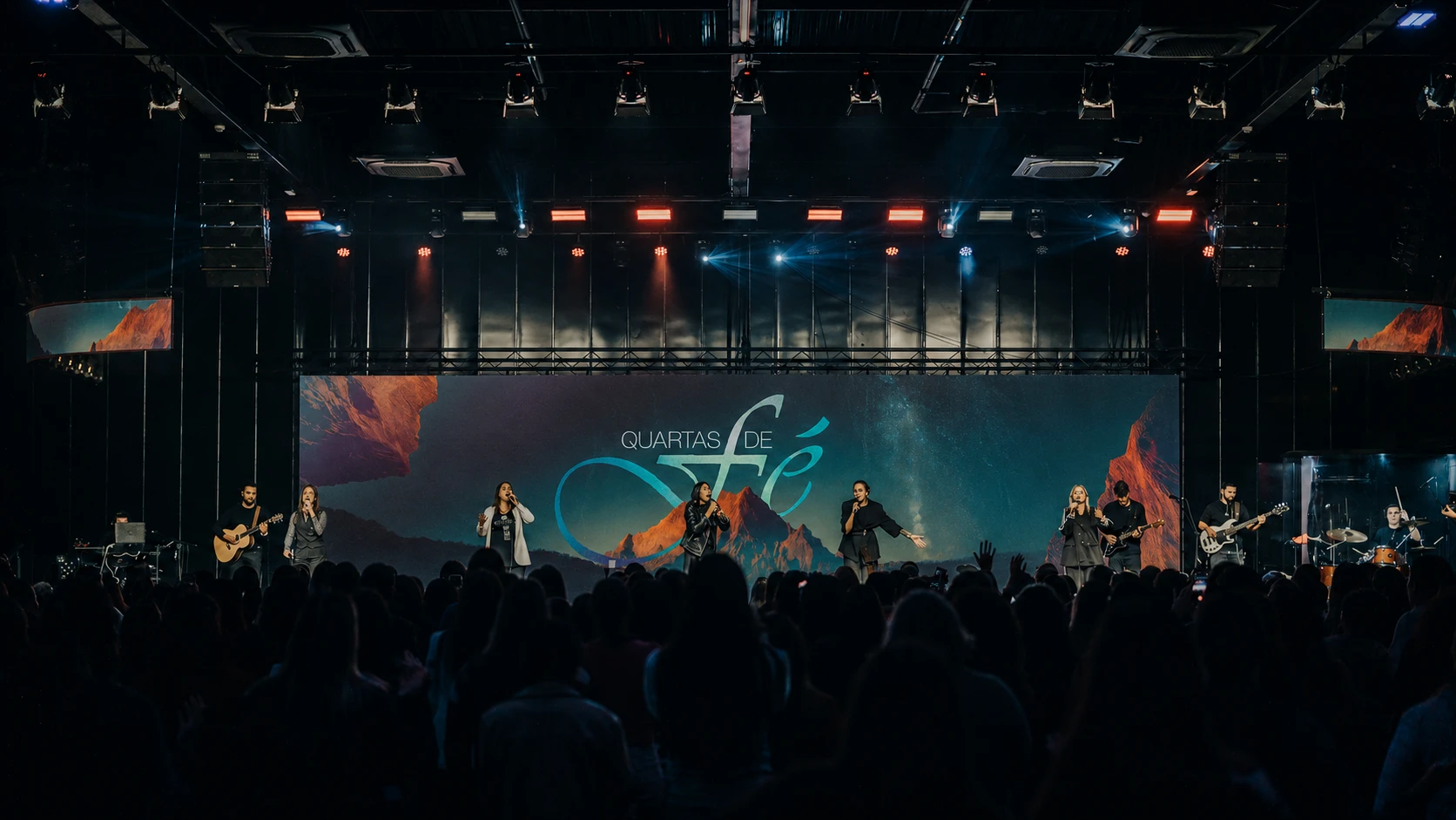Registro do encontro Quartas de Fé na igreja, com participantes no palco, público e identidade visual exibida no telão ao fundo.